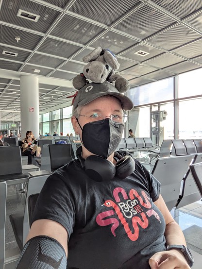 Me sitting in a waiting area at an airport, with a plush donkey on my head (and hat).