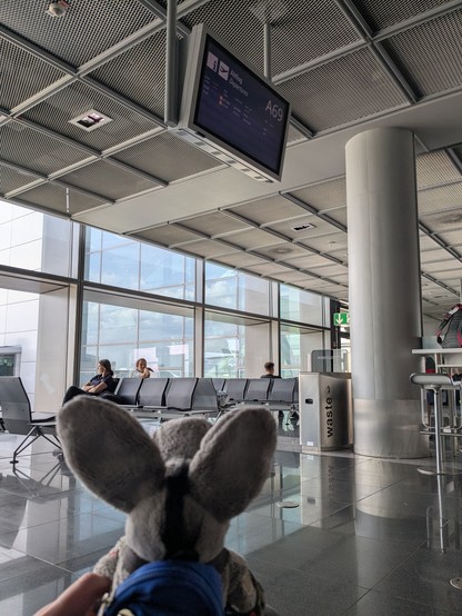 The plush donkey is looking up at a display at an airport. He's wearing a little backpack.