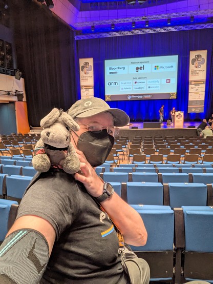 Selfie of me with my plush donkey Timothy on my shoulder, behind us a presentation stage