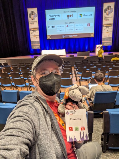 Selfie of me with plush donkey Timothy posing for the camera. Behind us the main stage of EuroPython 