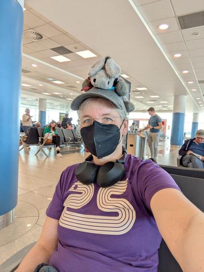 Me sitting at an airport gate, waiting for my flight, Timothy sitting on my head. I'm wearing the EuroPython 2025 t-shirt.