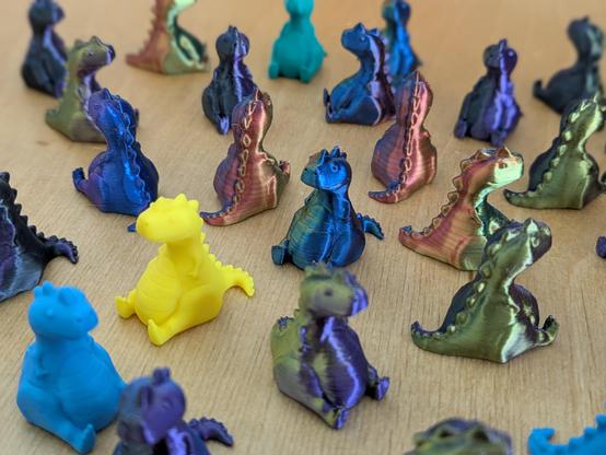 A closer look at tiny 3d printed chubby T-Rex models grouped together on a table showing off the different filament colors.