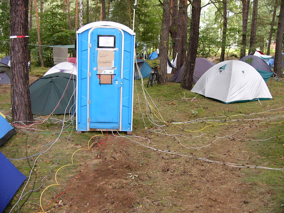 Ein blaues Datenklo mit Pappschildern und sehr vielen, oben und unten heraushängenden, vor allem hellgrauen Ethernetkabel in einem Kiefernwald mit vielen Igluzelten rundherum.

Bild vom Chaos Communication Camp in Finowfurt 2007

Quelle: Wikimedia/Flickr, https://commons.wikimedia.org/wiki/File:CCCamp_2007_Datenklo.jpg

Autor: RobotSkirts / Eliot Phillips

Lizenz:  Creative Commons Attribution-Share Alike 2.0 Generic