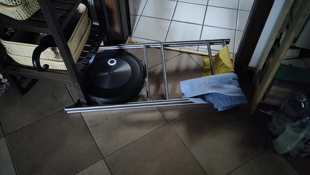 Staubsaugerroboter eingeklemmt in einem faltbaren Metalldings zum Lappentrocknen zwischen Regal und Türrahmen