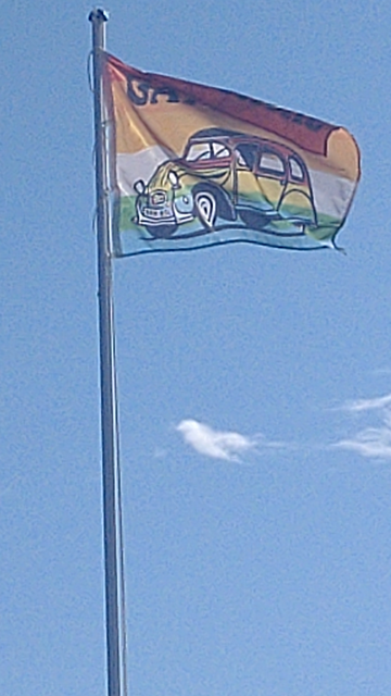 Eine Regenbogenflagge mit einem Comic-2CV in ebenfalls Regenbogenfarben. Darüber steht "GAY DUCKS".