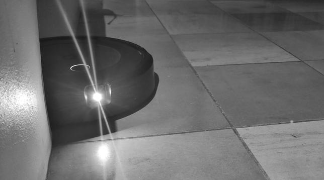 Ominous black and white picture of a Roomba vacuuming robot blinding the camera with its light