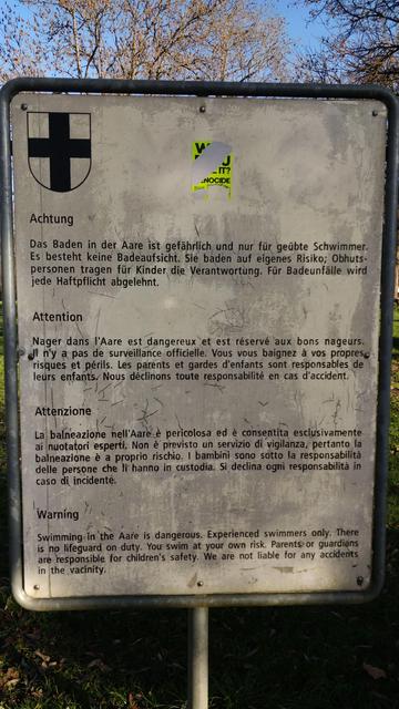 Schmutziges Schild, dass das Baden in der Aare auf Eigenrisiko geschieht in vier Sprachen.