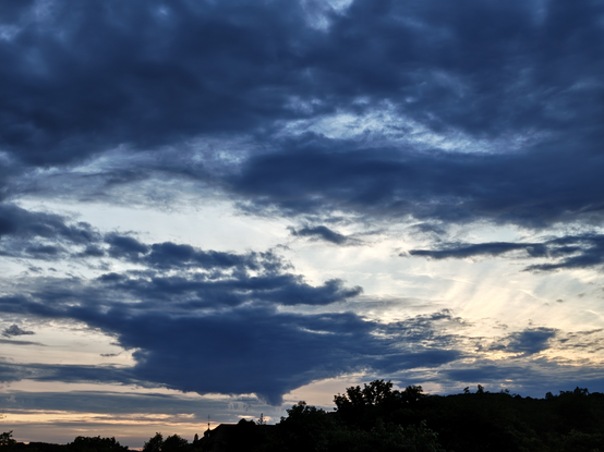 Dunkelblaue Wolken vor orange bis hellblauem Abendhimmel.